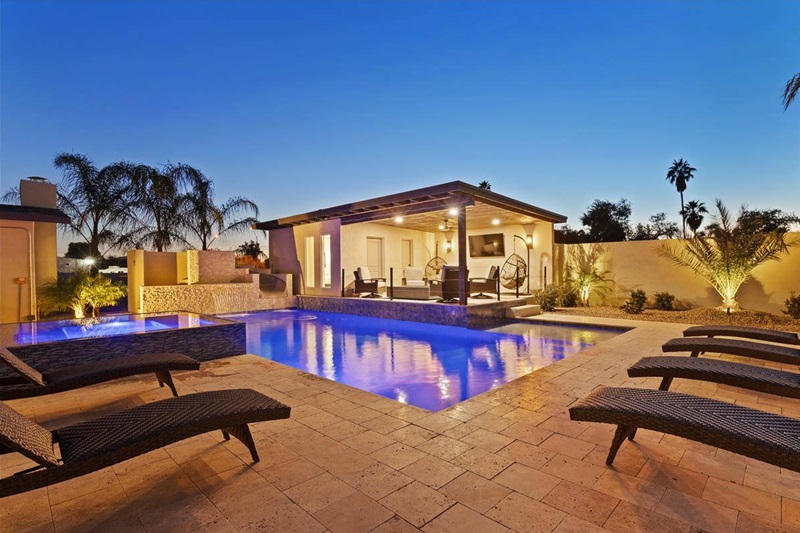 Scottsdale vacation home with a lit swimming pool, outdoor seating area, palm trees, and a clear evening sky.