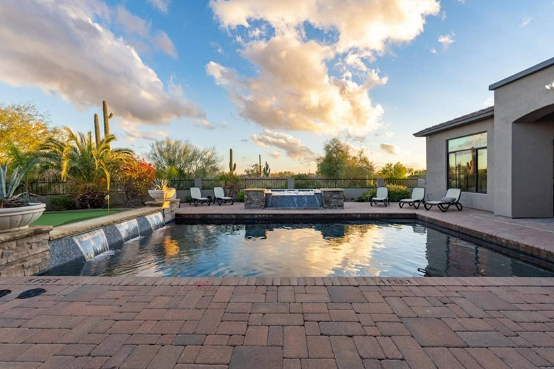 Luxury Scottsdale vacation home with a swimming pool, desert landscape, cacti, lounge chairs, and scenic sky view.
