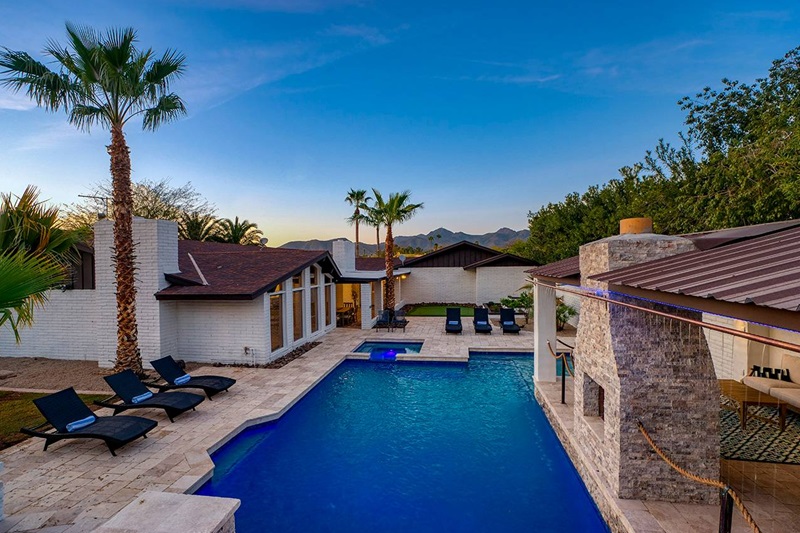 Luxury Scottsdale vacation home with a pool, palm trees, mountain views, and modern outdoor amenities at sunset.