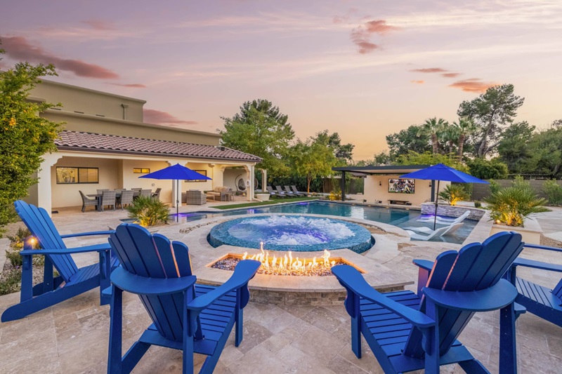 Luxury Scottsdale vacation home with a pool, hot tub, fire pit, outdoor dining, and lush landscaping at sunset.