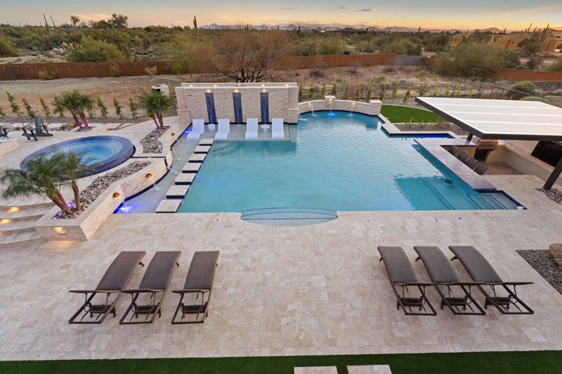 Luxury Scottsdale vacation home with a modern pool, hot tub, lounge chairs, and scenic desert views at sunset.