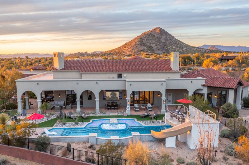 Luxury Scottsdale vacation home with a pool, hot tub, outdoor seating, and scenic mountain views at sunset.