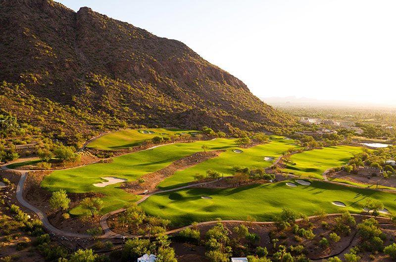 Scenic golf course in Phoenix/Scottsdale, Arizona, with lush green fairways, sand traps, and mountain backdrop at sunset.