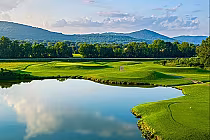 Scenic view of Hampton Cove Short Course golf course with lush green fairways, a water hazard, and mountains in the background.