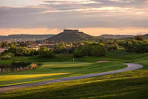 Scenic view of Plum Creek Golf Club with lush green fairways, a flag on the green, and a hill with a castle-like structure in the background.