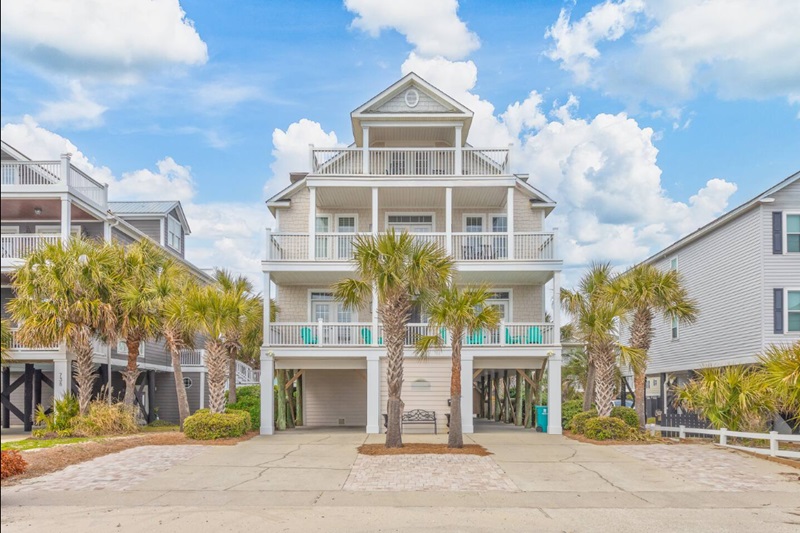 Pura Vida Beautiful 2nd row, 7-bedroom, 8-bathroom house in Garden City Beach with a private pool, multiple balconies, and palm trees.