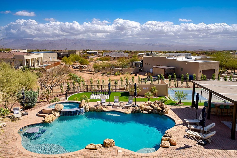 Scottsdale vacation home with a swimming pool, hot tub, lounge chairs, and desert landscape under a blue sky with clouds.
