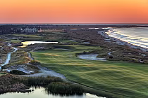 Scenic view of The Ocean Course at Kiawah Island featuring lush golf greens, sand dunes, water hazards, and ocean in the background at sunset.