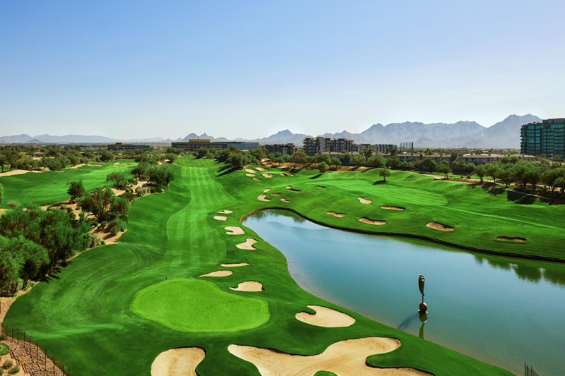 A scenic view of a lush golf course with sand traps, water hazards, and mountains in the background, near Scottsdale, AZ.