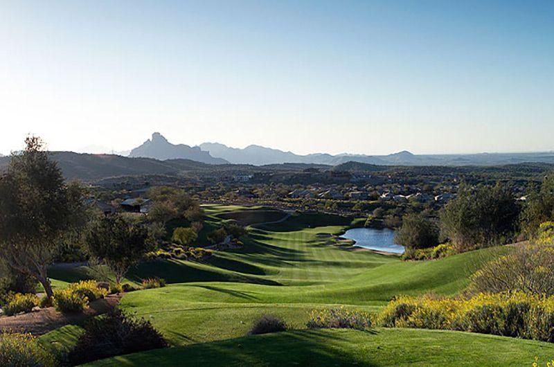 Scenic view of a lush golf course in Fountain Hills with rolling greens, water hazards, trees, and distant mountains under a clear sky.