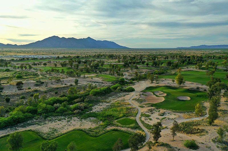 Aerial view of Southern Dunes golf course in Maricopa, Arizona, featuring lush green fairways, sand bunkers, and desert landscape with mountains in the background.