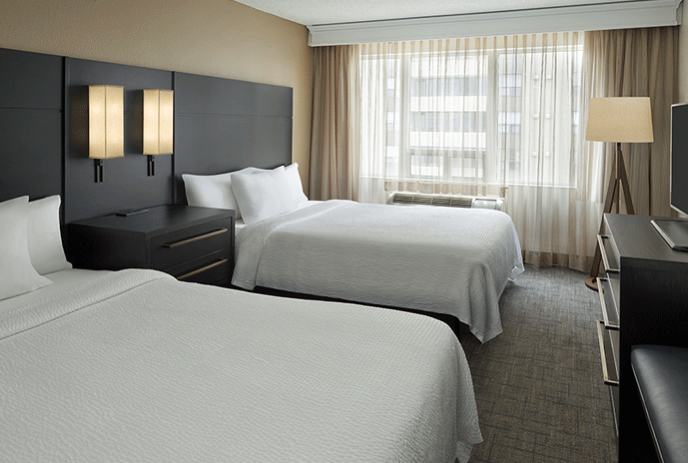 Residence Inn London Downtown Modern hotel room with two white beds, black headboards, bedside table, large window with curtains, and a TV.