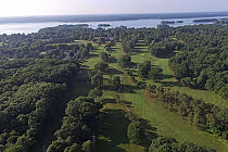 Aerial view of Brockville Country Club's lush, green 18-hole golf course with complex fairways, surrounded by trees and overlooking a lake.
