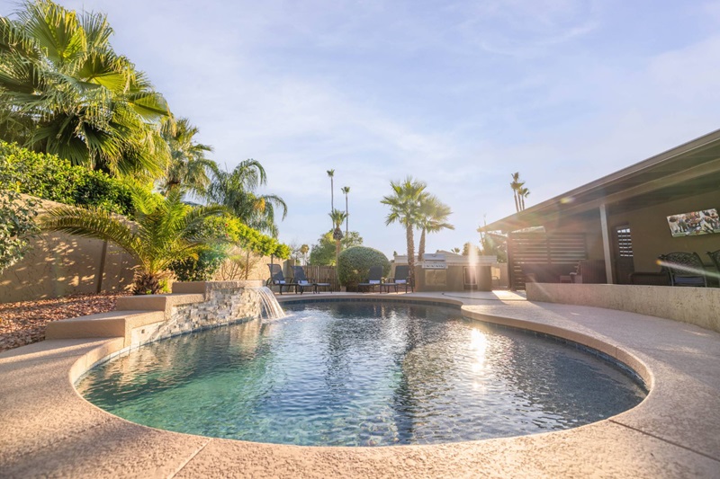 Luxurious Scottsdale vacation home with a pool, surrounded by palm trees, lush greenery, and a shaded outdoor lounge area.