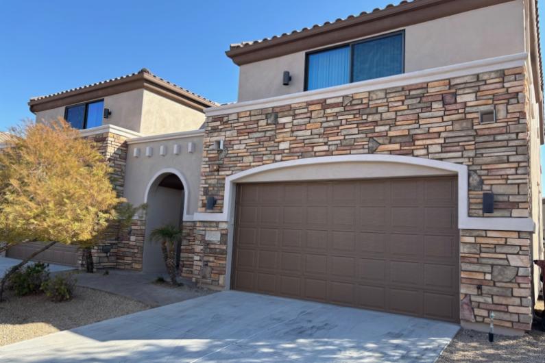 Modern two-story Scottsdale Townhomes with stone accents, a garage, and desert landscaping, set against a clear blue sky.