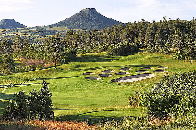 Scenic golf course in Colorado with lush green fairways, sand bunkers, surrounded by trees and mountains in the background.