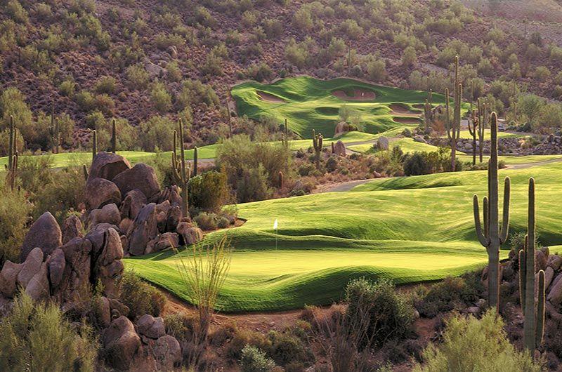 Scenic golf course in Phoenix/Scottsdale, AZ, featuring lush green fairways, desert rocks, and tall cacti in a desert landscape.