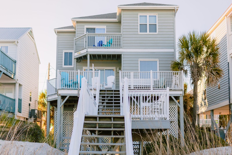 Paradise Sands Beachfront vacation home at Garden City Beach with multiple decks, outdoor furniture, and a palm tree, in a coastal setting.