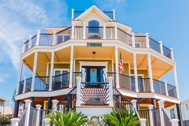 Palazzo 360 Colorful three-story house with balconies, black railings, and a staircase, under a blue sky, near the beach.