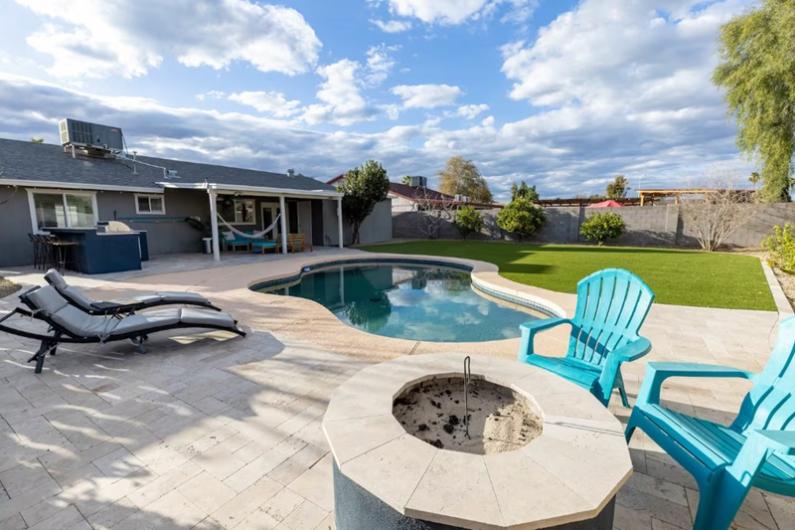 Beautiful backyard with a pool, lounge chairs, fire pit, and lush green lawn at Chandler Oasis, a golfer's paradise.