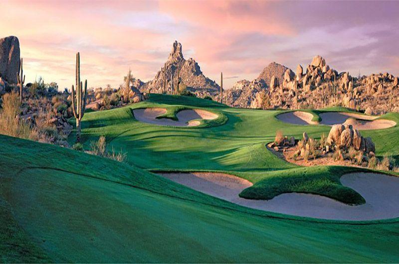 Scenic view of Troon North golf course with green fairways, sand traps, desert landscape, and rocky mountains at sunset in Scottsdale.