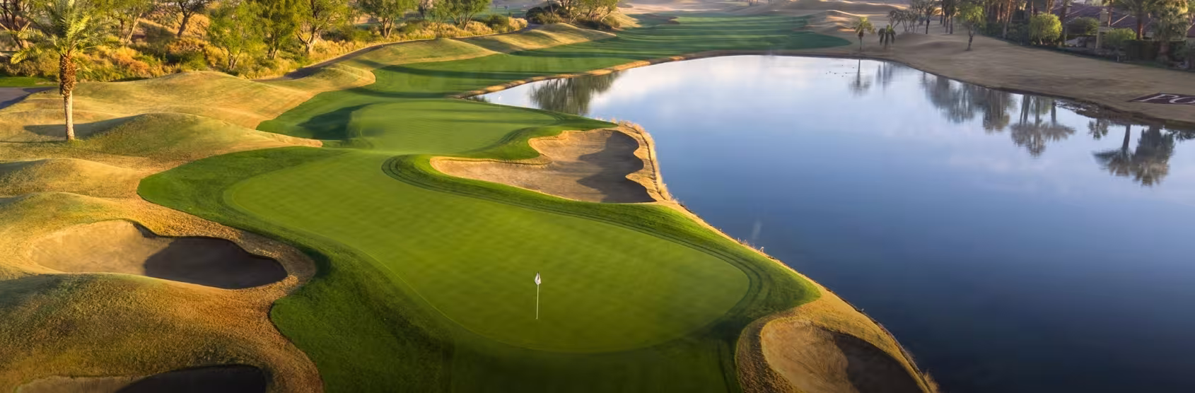 Aerial view of a lush golf course with green fairways, sand traps, water hazards, and surrounding trees in Southern California.