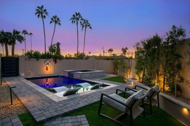 Luxurious Scottsdale backyard with a modern pool, lounge chairs, palm trees, and sunset sky, perfect for a golf vacation stay.