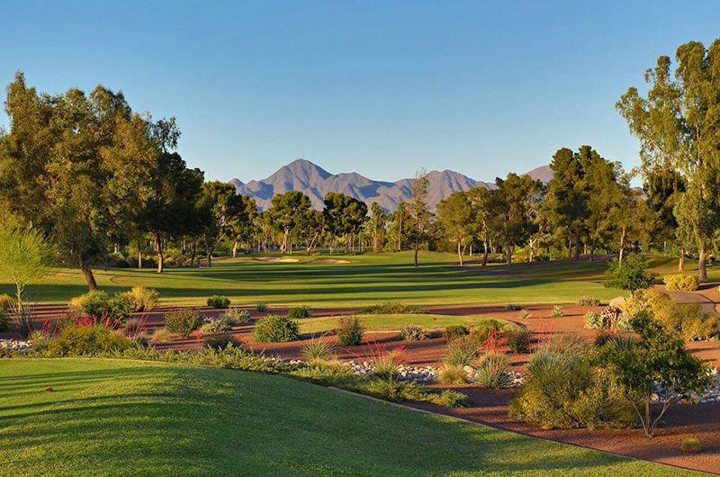 Scenic view of a golf course in Scottsdale, Arizona, with lush green fairways, trees, desert plants, and distant mountains under a clear blue sky.
