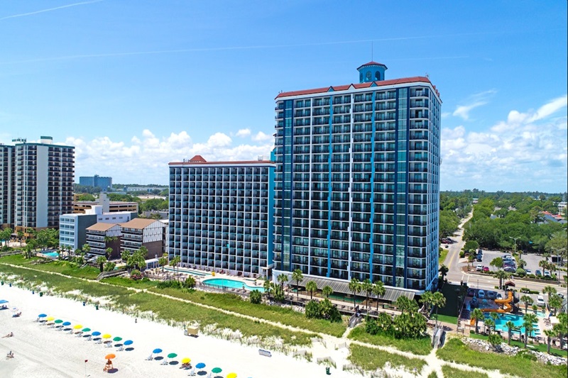 Caribbean Resort & Villas Luxury oceanfront resort with high-rise buildings, pools, and a sandy beach with colorful umbrellas in Myrtle Beach.