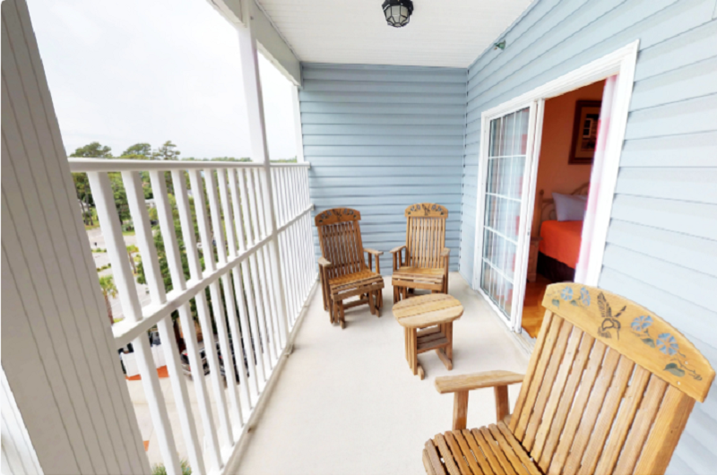 Myrtle Beach Villas - 302A Balcony of Myrtle Beach Villas 302A with wooden chairs and a small table, overlooking a green landscape and parking area.