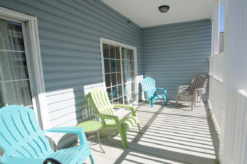 Myrtle Beach Villas - 304A Spacious Myrtle Beach condo balcony with colorful chairs, white railing, and sliding glass door, perfect for relaxing and golf trips.