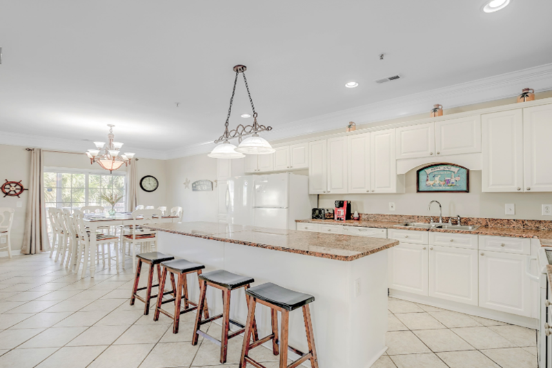 Bermuda Breeze - C Bright, spacious kitchen with white cabinets, granite countertops, and a breakfast bar with four stools, overlooking a dining area.