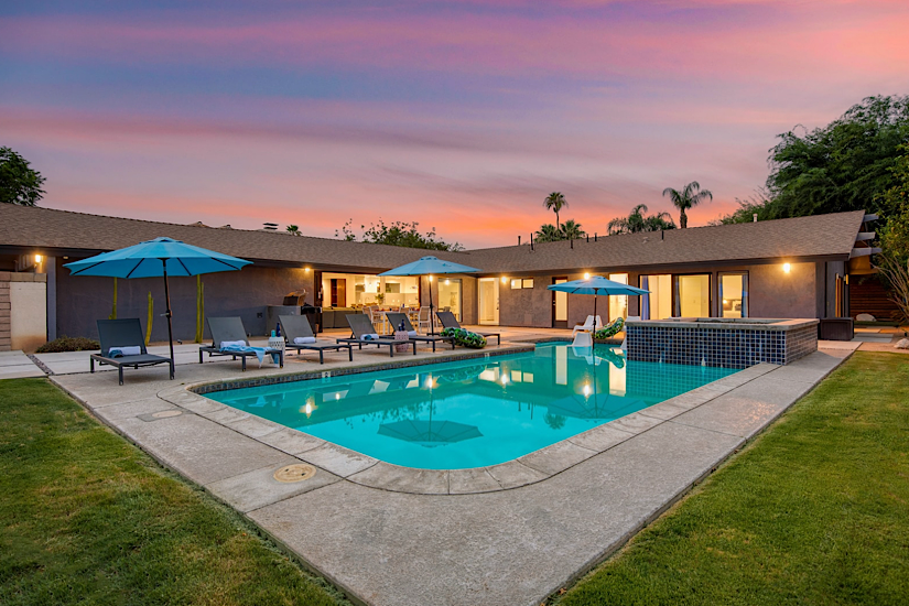 Quinta Blue & Green Luxury vacation home with a swimming pool, lounge chairs, umbrellas, and a sunset sky in La Quinta, California.