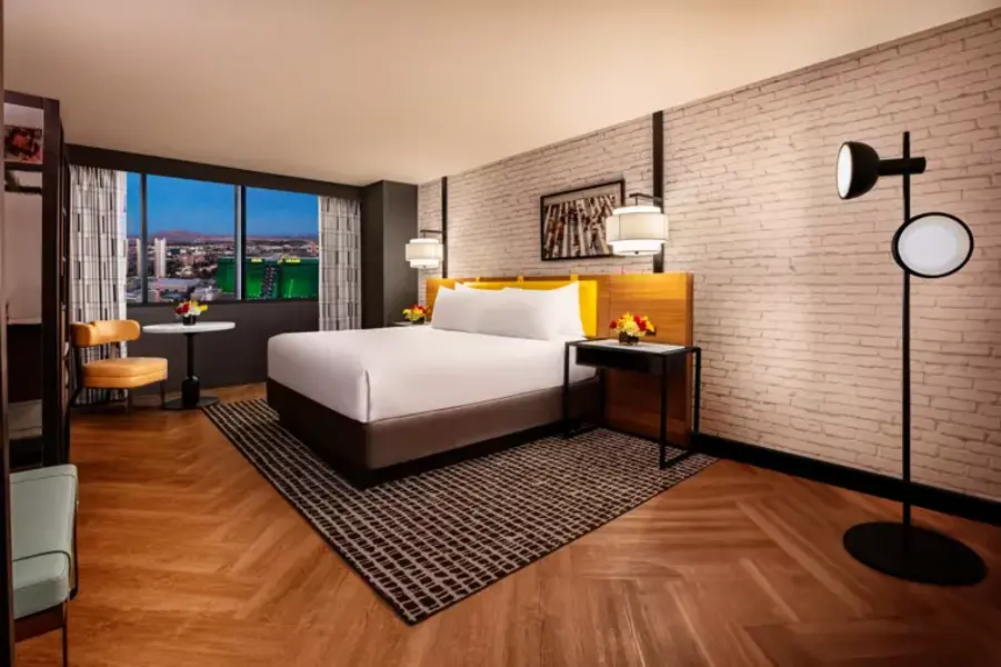 New York - New York Hotel & Casino Modern hotel room with a large bed, wooden headboard, stylish lighting, a small table with flowers, and city view from the window.