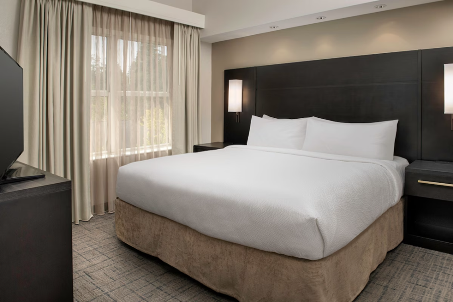 Modern hotel room at Residence Inn by Marriott Birmingham with a large bed, dark wood accents, and a window with curtains.