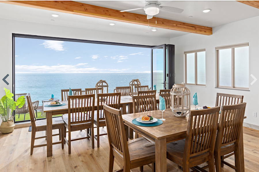 Bright dining room with wooden table and chairs, large ocean view through sliding glass doors, and natural light from windows.