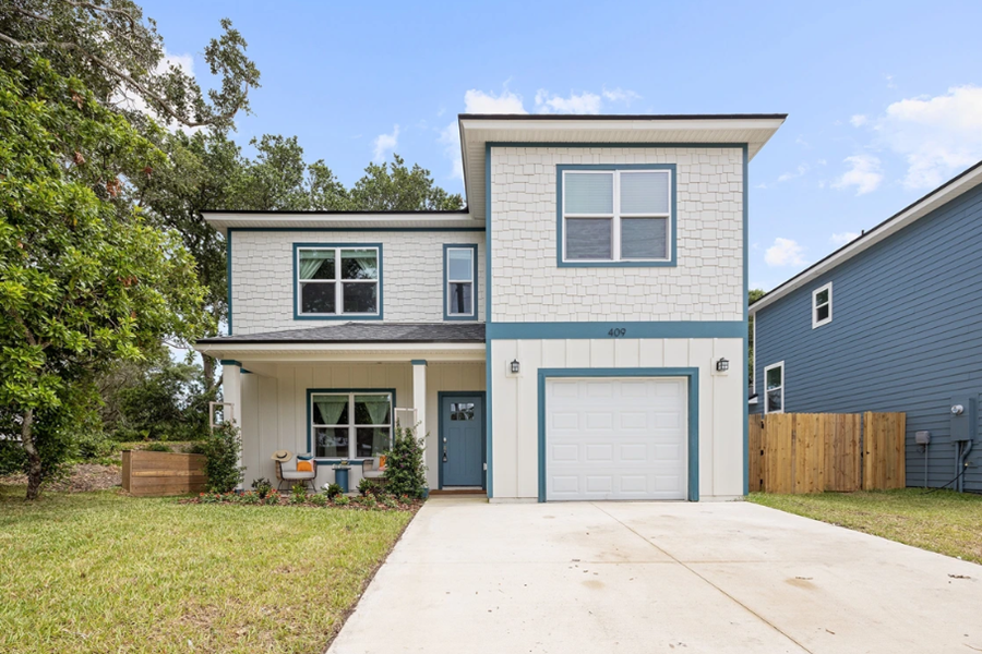 Luxury modern two-story home in St. Augustine with a backyard putting green, surrounded by trees and a clear blue sky.