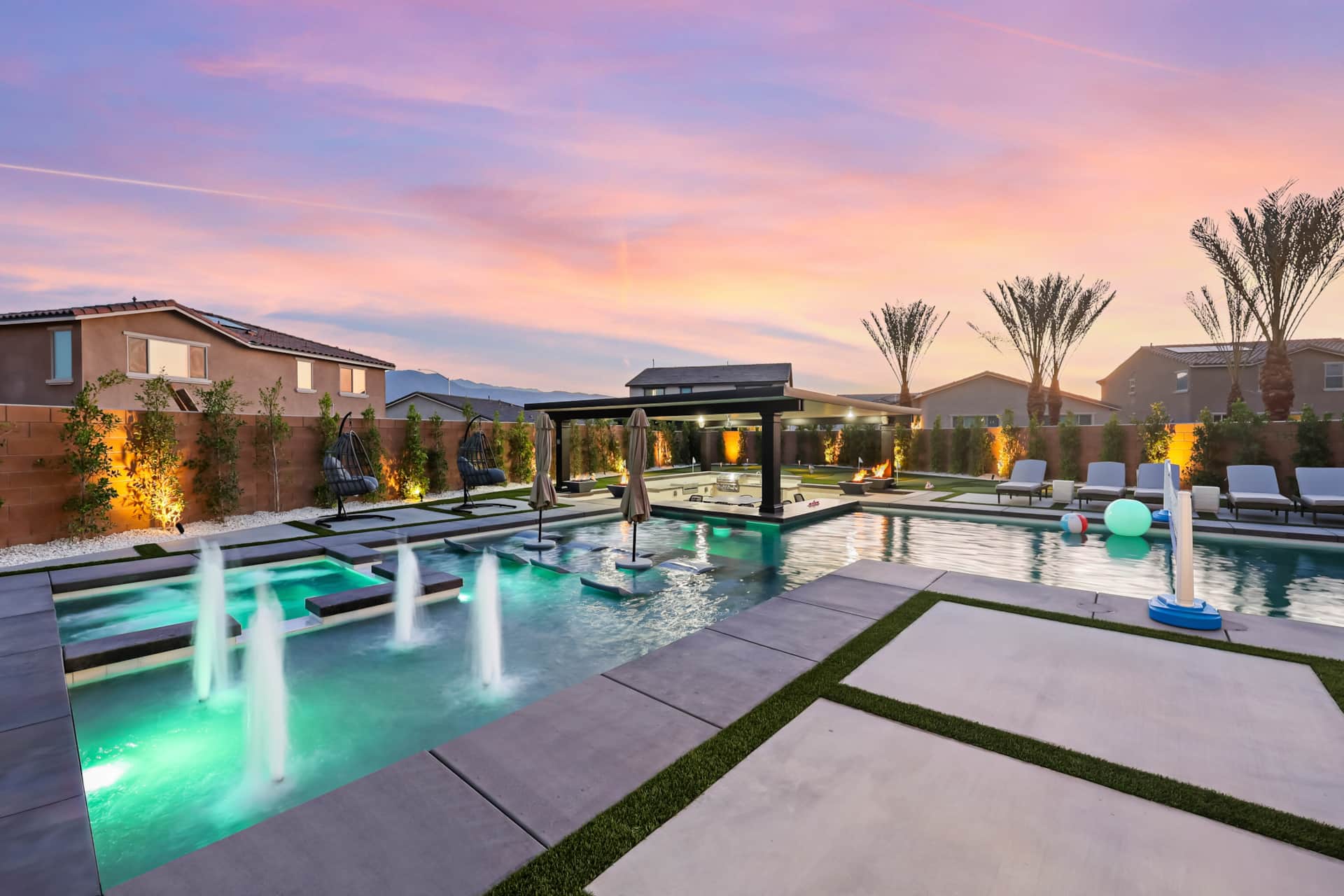 Desert Resort Game Room Heated SwimUpBar Geyser Luxurious desert resort pool area with swim-up bar, hot tubs, lounge chairs, and colorful floating balls at sunset.