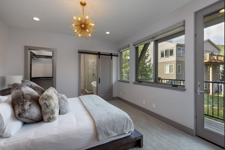 Modern bedroom with large windows, a sliding door to a balcony, and a view of neighboring houses in Keystone.