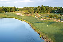 A scenic golf course with lush green fairways, sand traps, and a water hazard, surrounded by trees and blue sky.