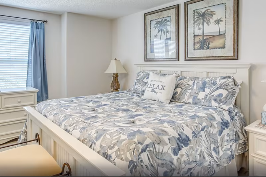 Barefoot Resort Golf Villa Cozy bedroom with a white bed, floral bedding, tropical art, and seaside decor, perfect for a relaxing vacation at Barefoot Resort.