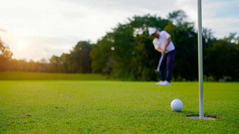 A golfer prepares to putt on a green with a golf ball near the hole and flagstick, during a sunny day at the golf course.