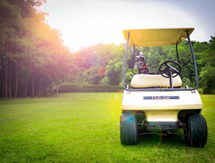 A white golf cart parked on a lush green golf course with trees in the background and sunlight shining through.