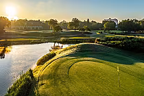 Scenic golf course in South Carolina with a green, flag, water hazard, trees, and a building in the background during sunset.