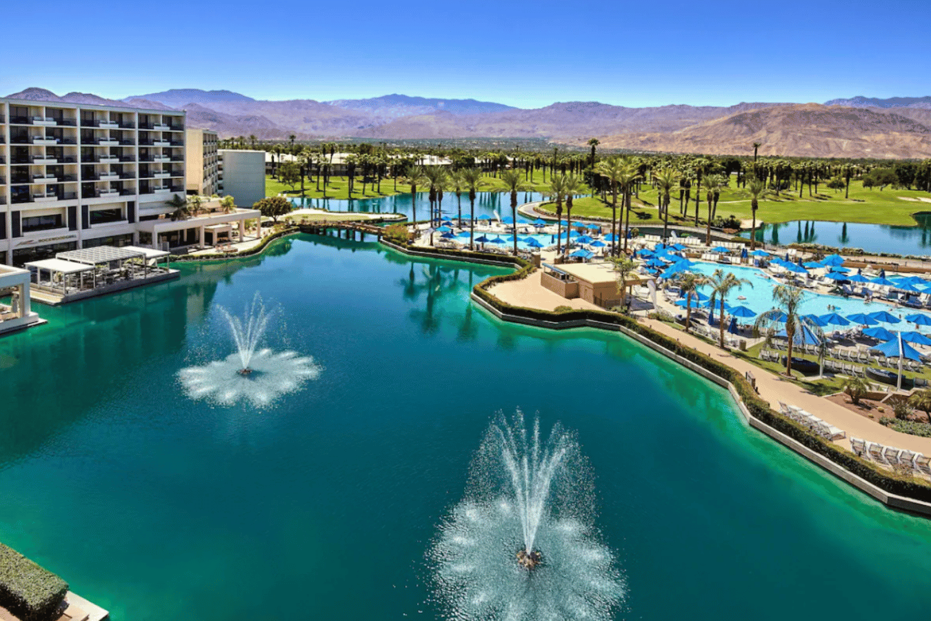 JW Marriott Desert Springs Resort & Spa Aerial view of JW Marriott Desert Springs Resort & Spa with large pool, fountains, palm trees, golf course, and mountain backdrop in Palm Springs.