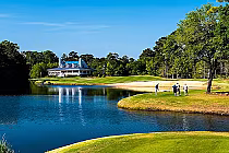 Golfers practice on a lush green course near a water hazard at True Blue Golf Club, a top-ranked public golf course in the US.