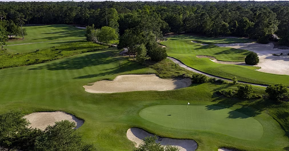 Aerial view of a lush golf course with sand bunkers, green fairways, and trees, near a private home with a pool in Myrtle Beach.