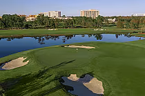 View of the Waldorf Astoria Golf Club in Orlando, featuring a green, sand bunkers, water hazard, and surrounding trees with hotel buildings in the background.