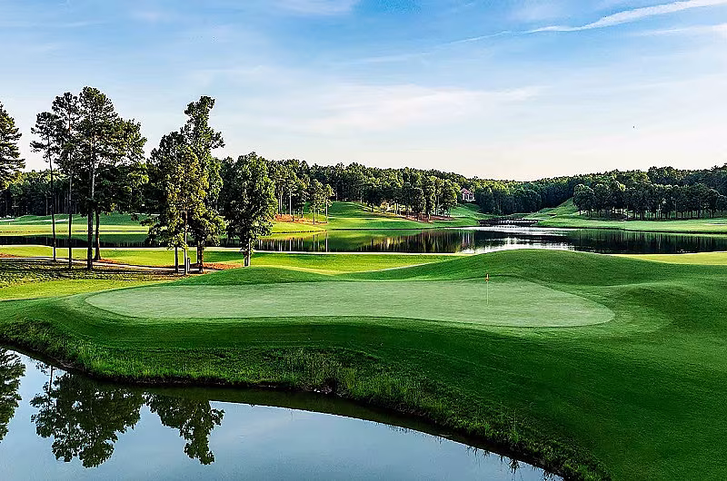 Scenic view of a golf course with green fairways, water hazards, trees, and a clear sky, part of the RTJ Ross Bridge stay and play package.
