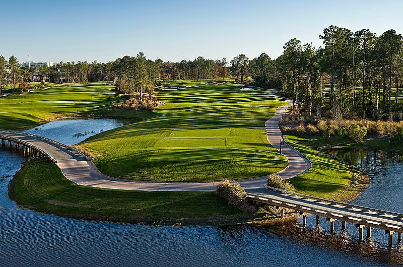 Scenic view of a golf course in Orlando, FL, with lush green fairways, water hazards, and a bridge, during daytime.